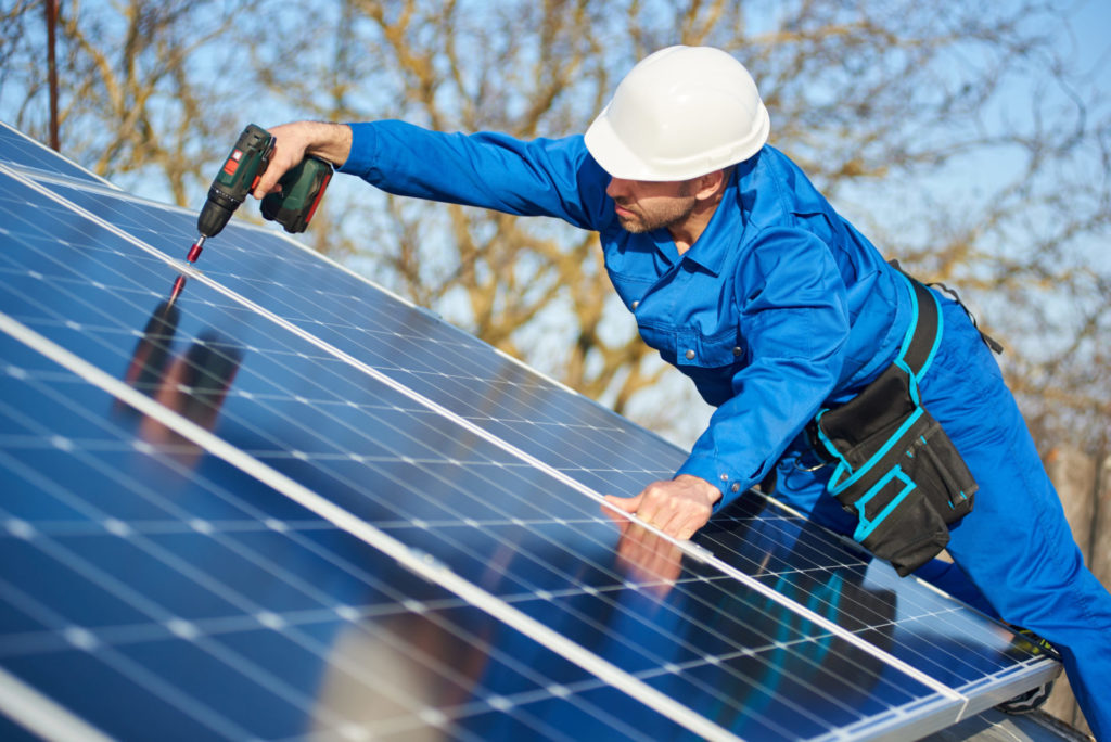 Electrician mounting solar panel on roof of modern house